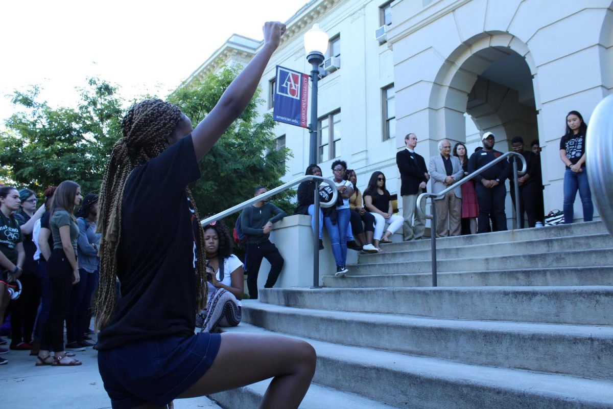 Student kneeling outside with a fist raised in the air outside of MGC during the rally.