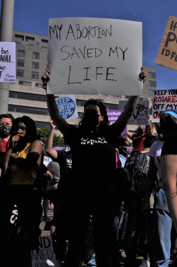 A protester raises a hand-written sign reading, “MY ABORTION SAVED MY LIFE.”